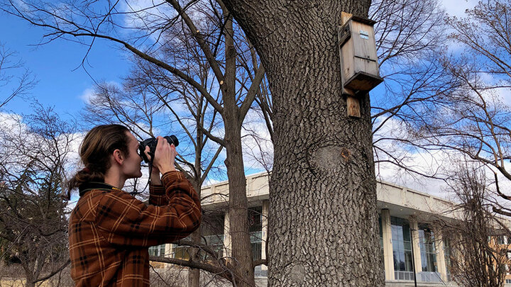 Josh Palik photographs a flying squirrel habitat house on campus.